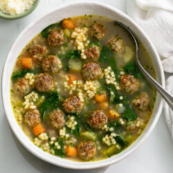 Italian Wedding Soup in a white bowl with a spoon.