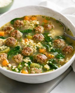 Italian Wedding Soup in a white bowl with meatballs and spinach.