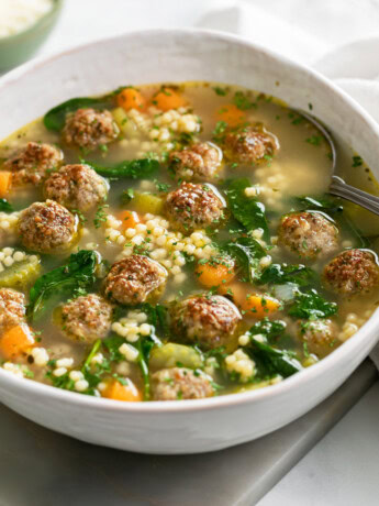 Italian Wedding Soup in a white bowl with meatballs and spinach.