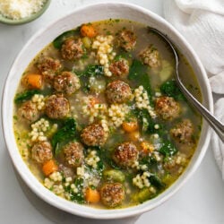 Italian Wedding Soup in a white bowl with a spoon on the side.