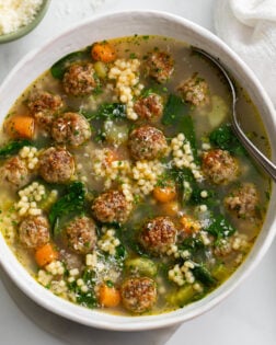 Italian Wedding Soup in a white bowl with a spoon on the side.
