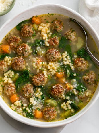 Italian Wedding Soup in a white bowl with a spoon on the side.