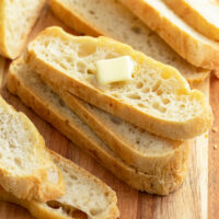 Slices of No Knead bread stacked on top of each other with butter on the top slice.