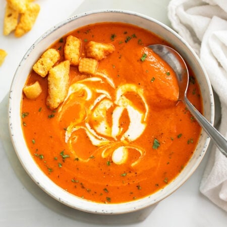 Roasted Red Pepper Soup in a white bowl with croutons and a swirl of cream.