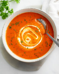 A bowl of Roasted Red Pepper Soup with cream swirled on top and a spoon on the side.