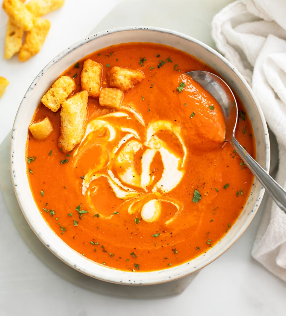 Roasted Red Pepper Soup in a white bowl with croutons and a swirl of cream.