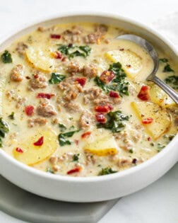 A white bowl of Zuppa Toscana Soup with bacon on top.