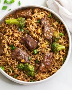 A white bowl with Ramen noodles and beef and broccoli in a brown sauce.