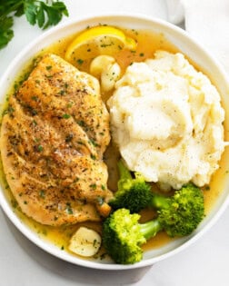 Pan Fried Chicken with pan sauce on a white plate with mashed potatoes and broccoli.