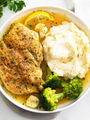 Pan Fried Chicken with pan sauce on a white plate with mashed potatoes and broccoli.