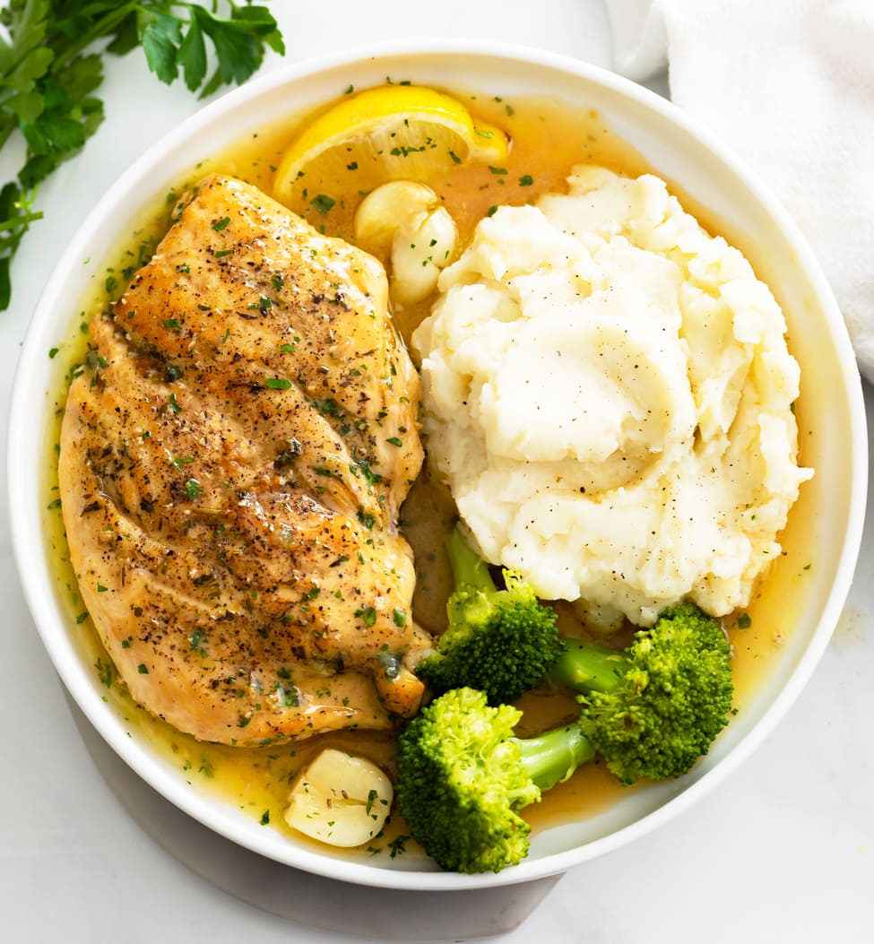 Pan Fried Chicken with pan sauce on a white plate with mashed potatoes and broccoli.
