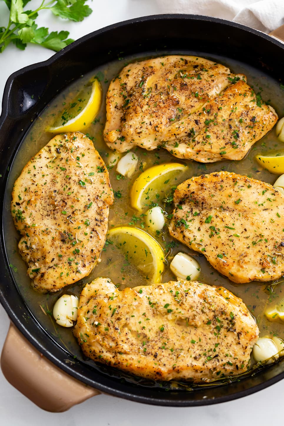 Pan Fried Chicken in a skillet with a pan sauce, lemons, garlic, and parsley.