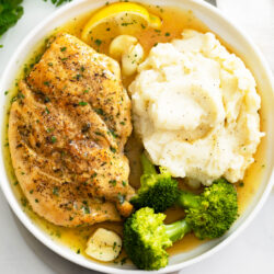Pan Fried Chicken on a white plate with broccoli and mashed potatoes.