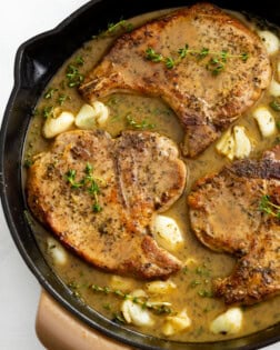 Pan Fried Pork Chops in a skillet with a pan sauce, garlic, and thyme.