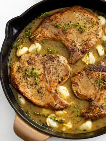 Pan Fried Pork Chops in a skillet with a pan sauce, garlic, and thyme.