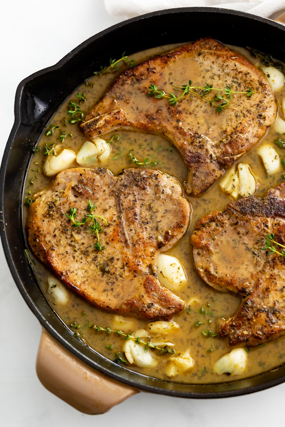 Pan Fried Pork Chops in a skillet with a pan sauce, garlic, and thyme.
