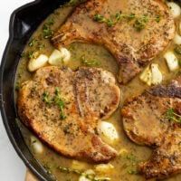 Pan Fried Pork Chops in a skillet with garlic, thyme, and pan sauce.