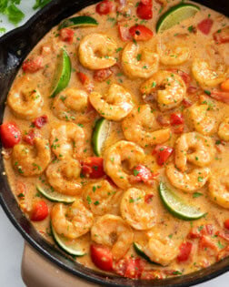 Cajun Shrimp in a skillet with sauce, bell peppers, and lime wedges.