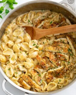 Creamy Chicken Pasta in a skillet with a wooden spoon and chopped parsley.