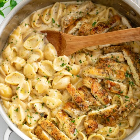 Creamy Chicken Pasta in a skillet with a wooden spoon and chopped parsley.