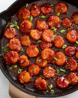 A skillet of Firecracker Shrimp with green onions and sesame seeds on top.