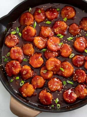 A skillet of Firecracker Shrimp with green onions and sesame seeds on top.