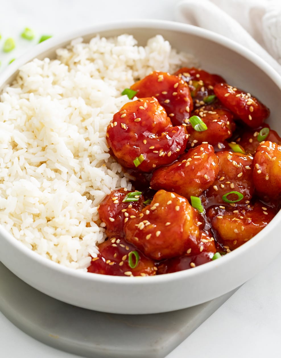 A white bowl with Firecracker Chickens next to a bed of white rice.