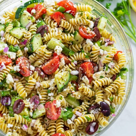 Greek pasta salad in a glass bowl with feta cheese on top.