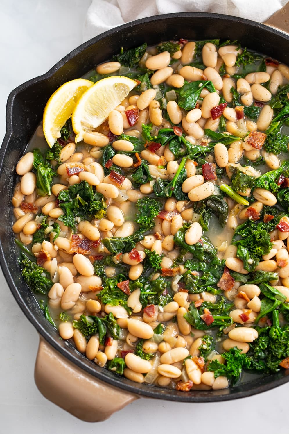 Greens and Beans in a skillet with bacon and freshly sliced lemon.