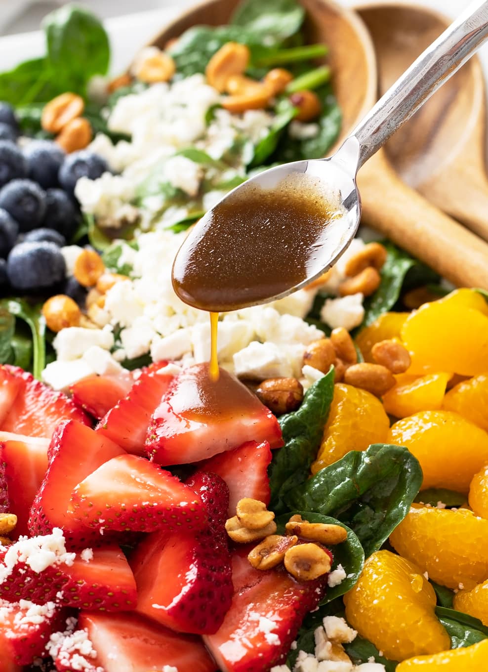 A spoonful of Balsamic Vinaigrette being drizzled onto a salad with spinach, strawberries, and feta.