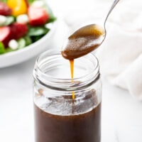 A spoon of Balsamic Vinaigrette being drizzled into a glass jar.