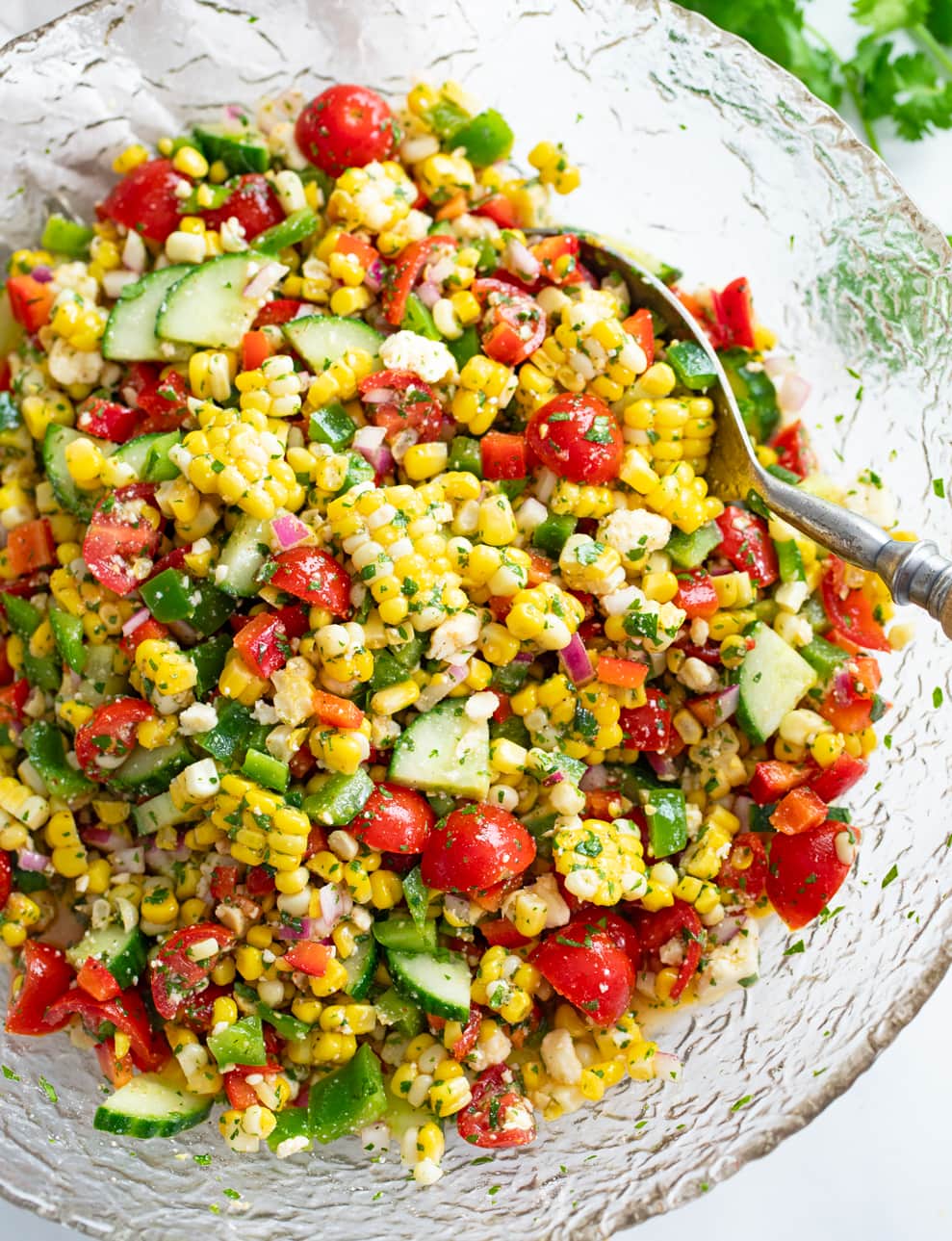 Overhead view of Corn Salad in a glass bowl with a spoon on the side.