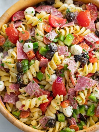 Italian Pasta Salad in a wooden bowl with spiral pasta, cheese, meat, and vegetables.