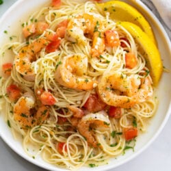 Shrimp Scampi on a white plate with angel hair pasta and a buttery white wine sauce.