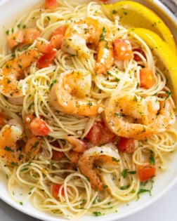 Shrimp Scampi on a white plate with angel hair pasta and a buttery white wine sauce.