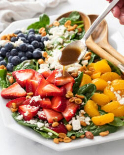 Spinach Salad on a white plate with a spoon drizzling Balsamic Vinaigrette on top.