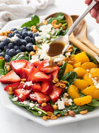 Spinach Salad on a white plate with a spoon drizzling Balsamic Vinaigrette on top.