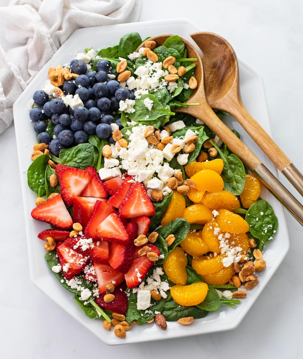 Spinach Salad on a white plate with fruit, peanuts, and feta cheese.