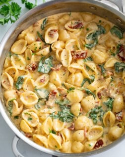 A skillet filled with creamy Tuscan Mac and Cheese with spinach and sundried tomatoes.