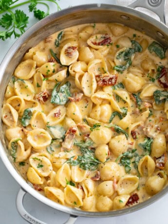 A skillet filled with creamy Tuscan Mac and Cheese with spinach and sundried tomatoes.