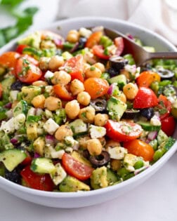 Chickpea Salad in a white bowl with Feta, cucumbers, tomatoes, olives, and dressing.