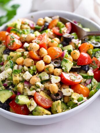 Chickpea Salad in a white bowl with Feta, cucumbers, tomatoes, olives, and dressing.