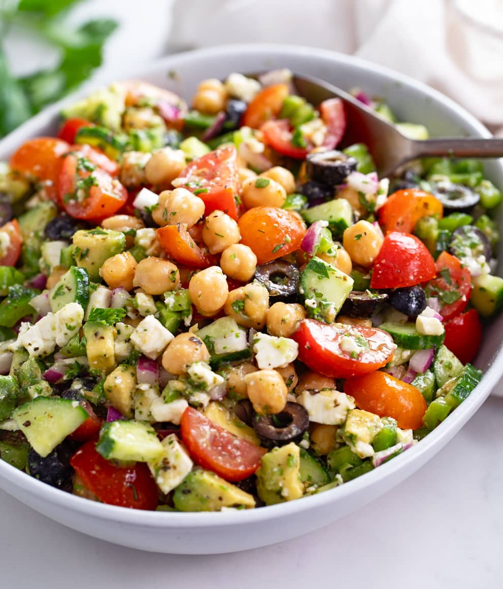 Chickpea Salad in a white bowl with Feta, cucumbers, tomatoes, olives, and dressing.