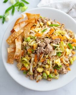 A white bowl filled with Egg Roll in a Bowl with crispy fried egg roll wraps on the side.