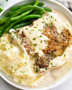 Ranch Pork Chops on a white plate with ranch sauce, potatoes, and green beans.