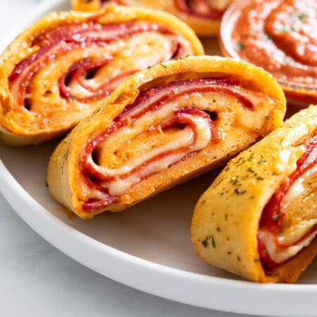 Stromboli with Italian cold cut filling on a white plate with Marinara sauce on the side.
