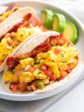 Breakfast Tacos filled with scrambled eggs, potatoes, and bacon on a white plate.