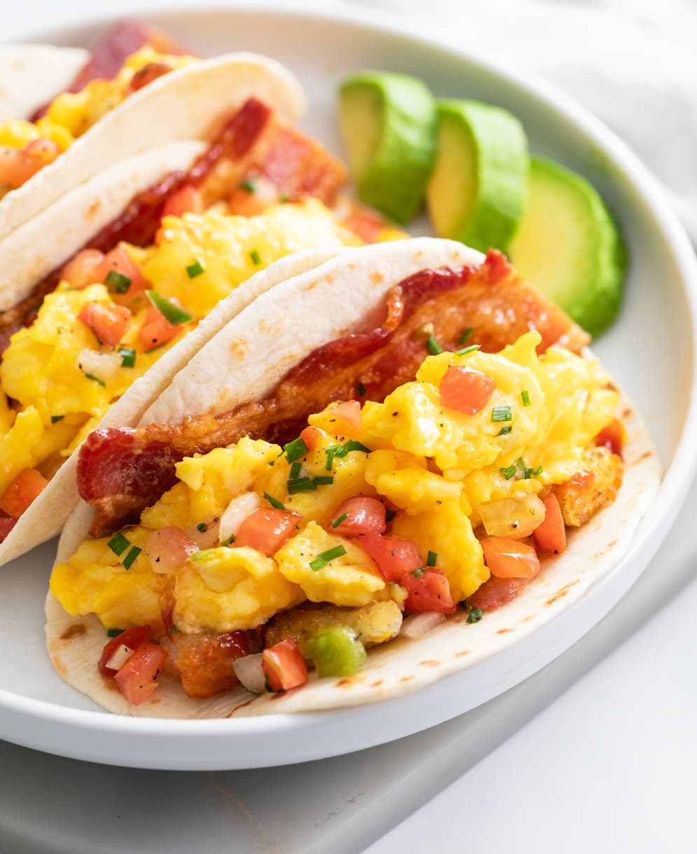 Breakfast Tacos filled with scrambled eggs, potatoes, and bacon on a white plate.