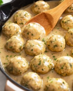 Chicken Meatballs in a skillet with sauce and a wooden spoon.