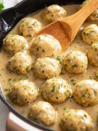 Chicken Meatballs in a skillet with sauce and a wooden spoon.